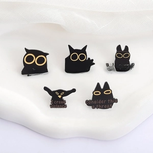 Detail of five funny black enamel pins featuring cats and birds with golden text