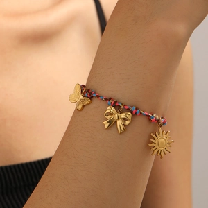 Détail d'un bracelet tissé avec breloques dorées soleil et papillon sur le poignet d'un mannequin