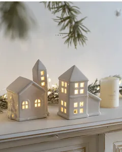 Detail of white ceramic Christmas house ornaments with warm glow and embossed pine trees