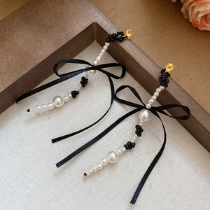 Detail of long bowknot tassel earrings with white pearls and black silk ribbon accents