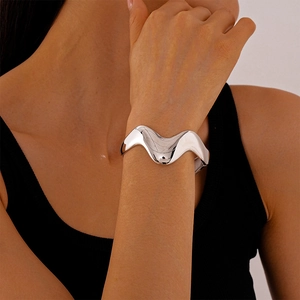 Detail of silver wavy open cuff bracelet on wrist showing glossy metallic finish