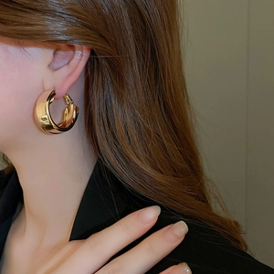 Detailed view of large gold-finish thick hoop earrings on model with polished mirror texture