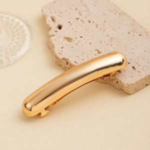 Polished gold curved hair clip on stone background with minimalist aesthetic detail