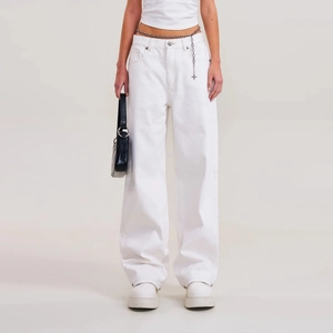 Détail d'un pantalon large en denim blanc avec une chaîne de taille en métal argenté stylée