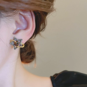 Detail view of retro gold Saturn earring with black star and crystal on model's ear
