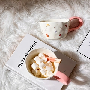 Top view of cream ceramic mugs with pink handles filled with sweets on white faux fur rug