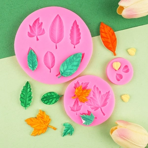 Pink silicone maple leaf fondant molds with colorful resin leaf decorations on a green base