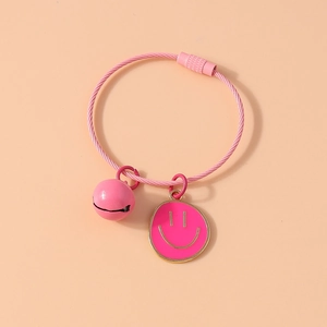 Macro detail of a pink wire bracelet with a bell and golden-edged smiley face pendant