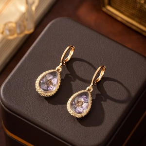 Macro shot of gold teardrop earrings with preserved purple dried flowers inside glass