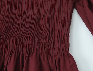Détail macro du tissu plissé nid d'abeille bordeaux avec texture élastique sur chemise