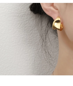 Close-up of minimalist streamlined gold stud earrings worn by a model in soft light