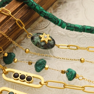 Detail of beaded bracelets featuring green malachite stones and golden chain elements