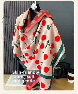 Close-up of thick beige cashmere scarf with red cherry patterns and soft fringe detail