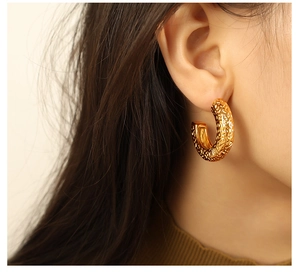 Detail shot of golden C-shaped hammered texture stud earrings worn by a model