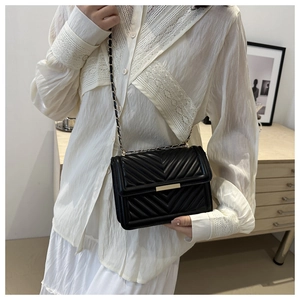 Close-up of black herringbone quilted crossbody bag with gold chain strap on model