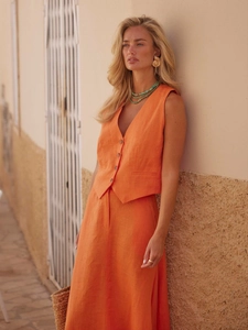 Detail of orange linen vest set with V-neck and buttons against a sunny stone wall