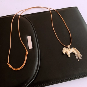 Detail view of a golden horse pendant with tassel fringe on a brown woven necklace cord