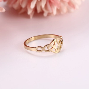 Detailed view of gold Triquetra Celtic knot ring with elegant floral pink background