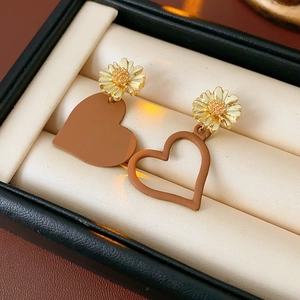 Macro shot of asymmetrical daisy earrings with brown heart charms on beige velvet display
