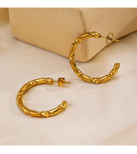 Macro detail of 18K gold plated C-shape earrings with twisted texture and butterfly backing