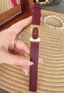 Elegant red leather watch with rectangular gold case held against a lifestyle background