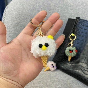 Hand-held close-up of a cute white plush ice cream cone keychain with cartoon eyes