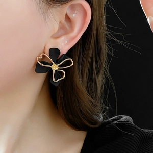 Close-up of black hollow flower earrings with gold edges on model's ear in soft lighting