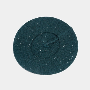 Close-up of deep teal knitted beret with sparkling silver sequins and soft wool texture