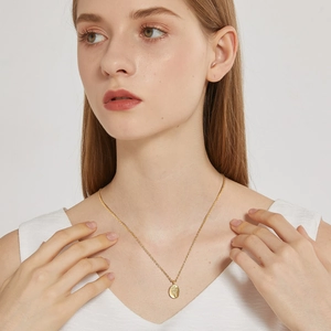 Close-up of a gold necklace with an oval rose relief pendant worn by a model