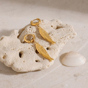 Detailansicht goldener Fischohrringe auf Korallenstein mit Strand- und Meeres-Ästhetik