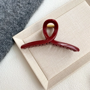 Close-up of deep red resin hair claw clip with golden metal spring on a beige tray
