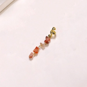 Detail of a gold ear cuff with irregular reddish-brown natural stone tassel pendants
