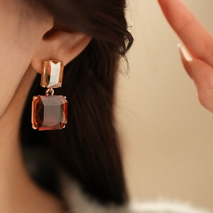 Dettaglio degli orecchini pendenti geometrici color ambra e marrone indossati da modella