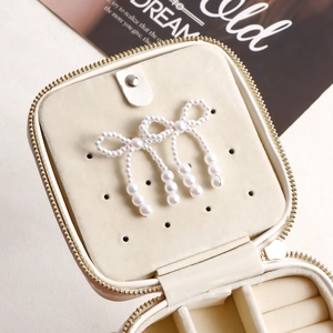 Close-up of white imitation pearl bow earrings inside a chic cream jewelry storage box