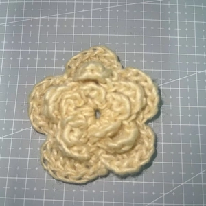 Detailed close-up of a 7cm triple-layered beige crochet flower with yarn texture