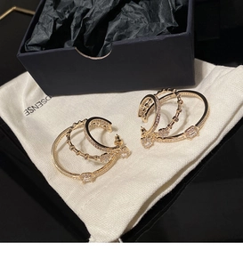 Close-up of golden triple-layered hoop earrings with zircons on a beige jewelry pouch