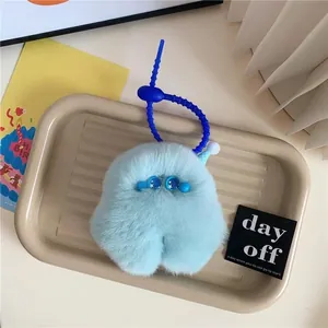 Cute light blue plush monster keychain with star eyes and mini hat on a beige tray