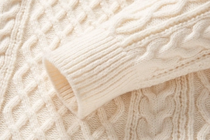 Vista macro della maglia a trecce e polsini a coste sul maglione bianco crema