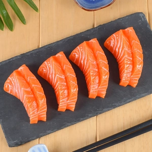 Gros plan de quatre tranches de sashimi de saumon réalistes en PVC sur une ardoise