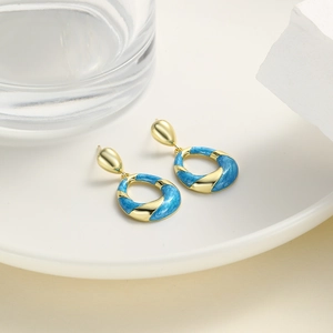 Detailed close-up of golden and sky blue enamel twisted geometric drop earrings on white decor