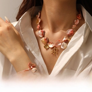 Detail of gold starfish and coral charms on layered shell beaded necklace and bracelet