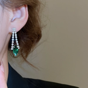 Detail of luxury teardrop earring with green gemstone and silver tassel chain on model