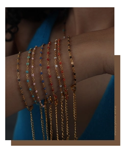 Nahaufnahme von goldener Gliederkette mit bunten Perlen im Set zum Layering am Handgelenk