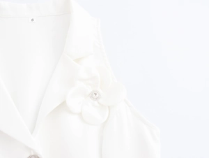 Close-up of elegant white vest featuring a large 3D fabric flower with rhinestone detail