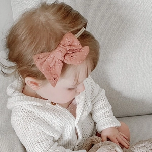 Detailed view of pink embroidered bow headband on baby girl in a home setting