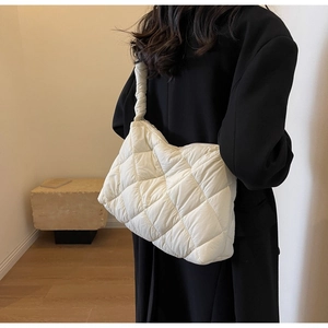 Detail view of the white quilted puffy shoulder bag worn on a shoulder for scale
