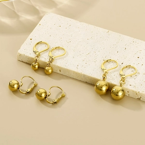Detail of polished gold steel ball drop earrings with lever-back clasp on stone surface