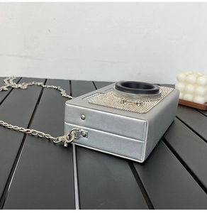 Detailopname van een zilveren schoudertas in cameravorm met strass op een gestreepte tafel