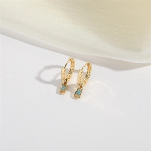 Detail of luxury gold zipper-shaped earrings with turquoise stones and silk background