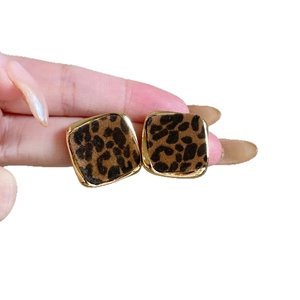 Leopard print square stud earrings with gold metal frame held by hand on white background